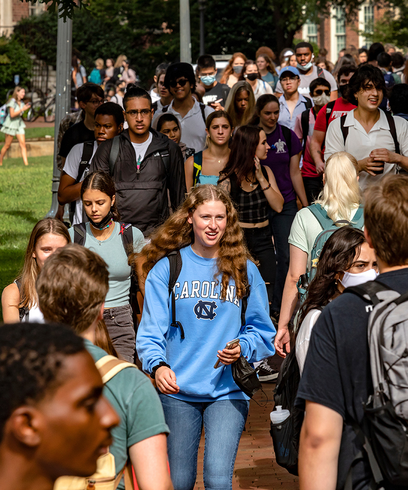 Students walk on campus, in the center is a woman wearing a UNC sweatshirt